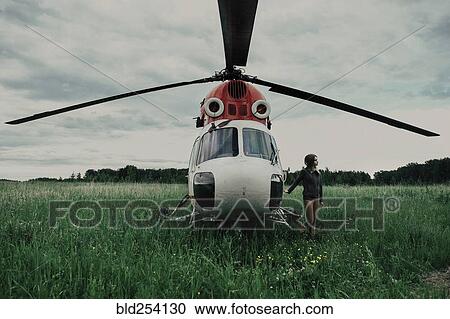 Stock Image - Caucasian woman standing near helicopter in field. Fotosearch
