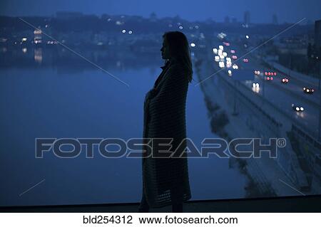 Stock Image - Caucasian woman standing near waterfront at night. Fotosearch
