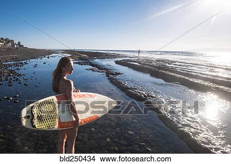 Picture - Caucasian woman standing on beach holding surfboard. Fotosearch