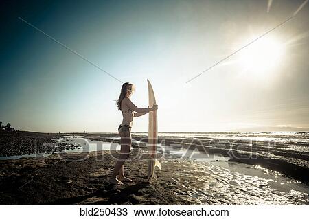 Caucasian woman standing on beach holding surfboard View Large Photo Image Stock Image - Caucasian woman standing on beach holding surfboard. Fotosearch