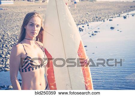 Caucasian woman standing on beach holding surfboard View Large Photo Image Stock Photo - Caucasian woman standing on beach holding surfboard. Fotosearch
