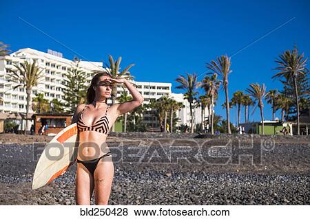 Stock Photo - Caucasian woman standing on beach holding surfboard. Fotosearch