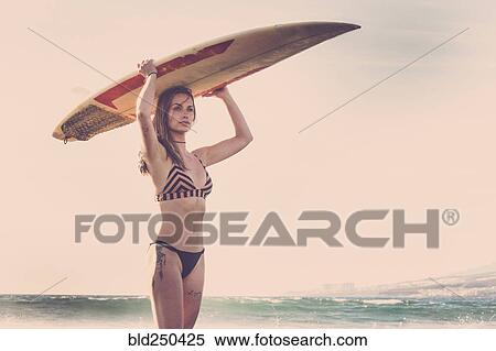 Stock Photography - Caucasian woman standing on beach holding surfboard. Fotosearch