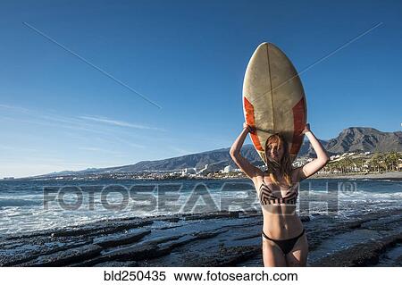 Stock Photography - Caucasian woman standing on beach holding surfboard. Fotosearch