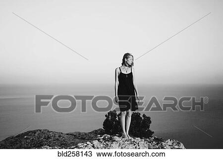 Stock Image - Caucasian woman standing on rock near ocean. Fotosearch