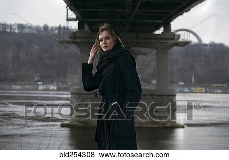 Stock Photo - Caucasian woman standing under bridge near river. Fotosearch