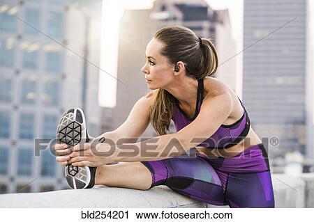 Stock Image - Caucasian woman stretching leg on urban rooftop. Fotosearch