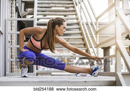 Stock Photo - Caucasian woman stretching leg on urban staircase. Fotosearch