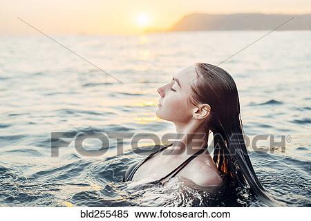 Stock Photography - Caucasian woman swimming at sunset. Fotosearch