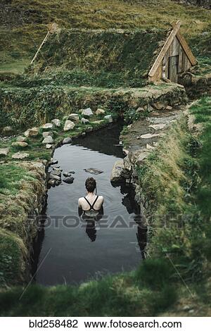 Stock Image - Caucasian woman swimming in pond near rural house. Fotosearch