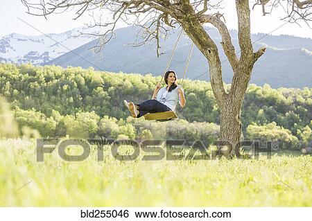 Stock Photograph - Caucasian woman swinging on tree swing. Fotosearch