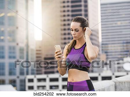 Stock Image - Caucasian woman texting on cell phone on urban rooftop. Fotosearch