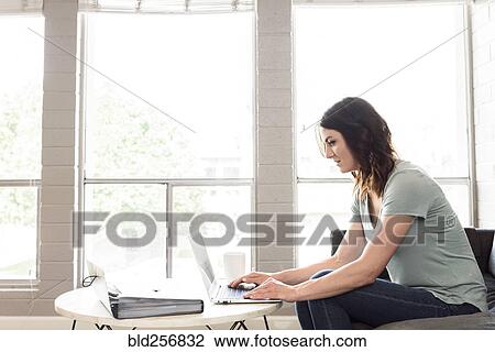 Stock Image - Caucasian woman using laptop on sofa. Fotosearch