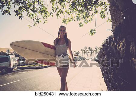 Caucasian woman walking on sidewalk carrying surfboard View Large Photo Image Stock Image - Caucasian woman walking on sidewalk carrying surfboard. Fotosearch