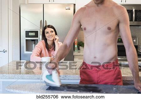 Stock Photograph - Caucasian woman watching man ironing shirt. Fotosearch