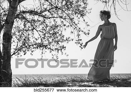 Stock Photo - Caucasian woman wearing a dress near tree. Fotosearch