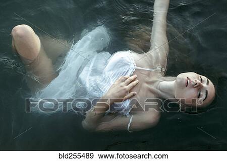 Stock Photo - Caucasian woman wearing a dress floating in water. Fotosearch