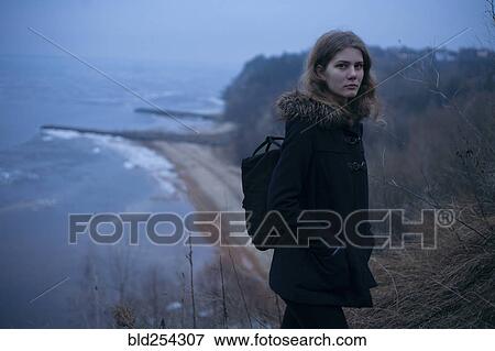 Stock Photo - Caucasian woman wearing coat on cliff near ocean. Fotosearch