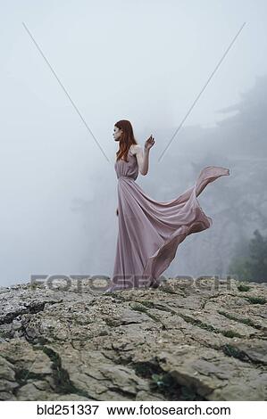 Stock Photo - Caucasian woman wearing dress on rock in fog. Fotosearch