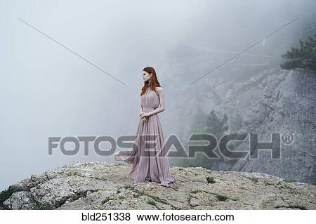 Stock Photo - Caucasian woman wearing dress on rock in fog. Fotosearch