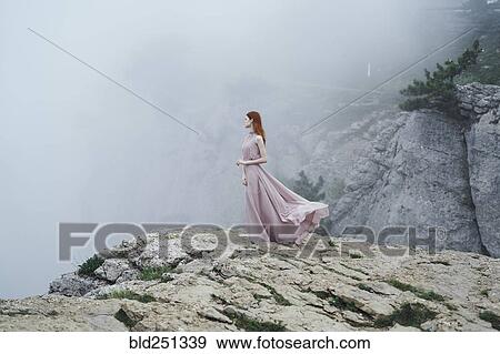 Stock Photo - Caucasian woman wearing dress on rock in fog. Fotosearch