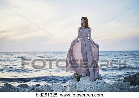 Stock Photography - Caucasian woman wearing dress on rocks near ocean. Fotosearch