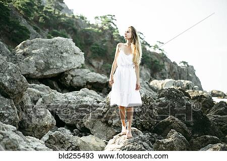 Stock Image - Caucasian woman wearing dress standing on rocks. Fotosearch
