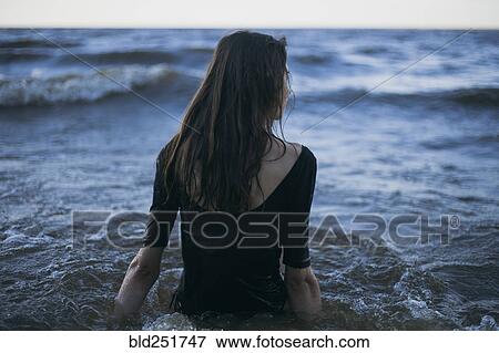 Stock Photo - Caucasian woman wearing dress wading in ocean. Fotosearch