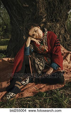 Picture - Caucasian woman wearing traditional clothing sitting near tree. Fotosearch