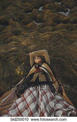 Stock Image - Caucasian woman wearing traditional clothing laying in grass. Fotosearch
