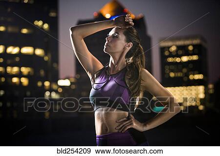 Stock Photo - Caucasian woman wiping forehead in city at night. Fotosearch