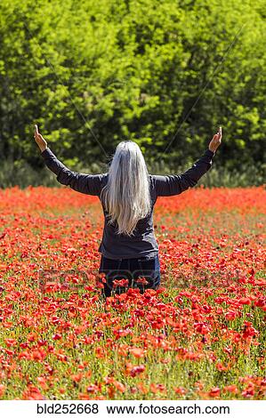 Stock Photo - Caucasian woman with arms raised in field of flowers. Fotosearch