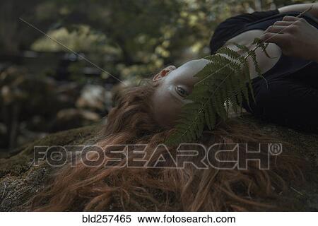 Stock Photography - Caucasian woman with red hair hiding face behind leaf. Fotosearch