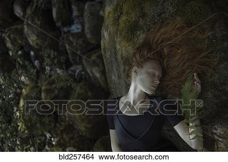 Picture - Caucasian woman with red hair laying on rock. Fotosearch