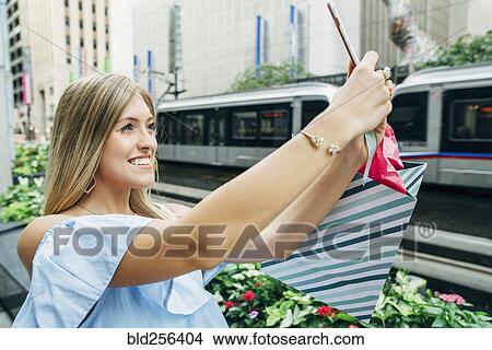 Caucasian woman with shopping bag posing for cell phone selfie View Large Photo Image Picture - Caucasian woman with shopping bag posing for cell phone selfie. Fotosearch