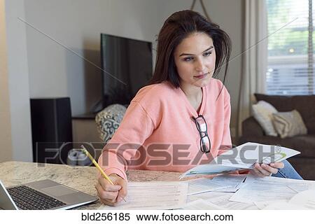 Stock Photography - Caucasian woman writing on paperwork near laptop. Fotosearch