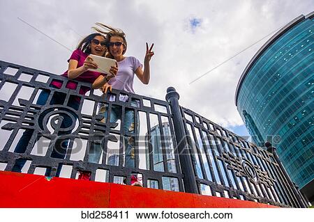 Stock Image - Caucasian women posing for selfie near railing using digital tablet. Fotosearch