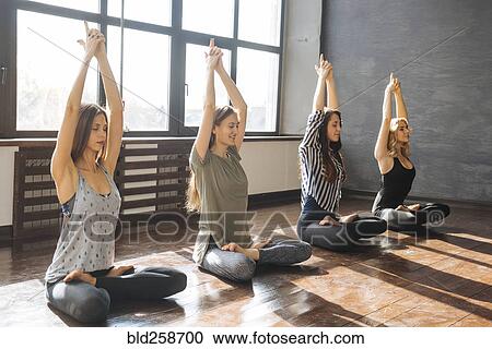 Stock Image - Caucasian women stretching arms in yoga class. Fotosearch