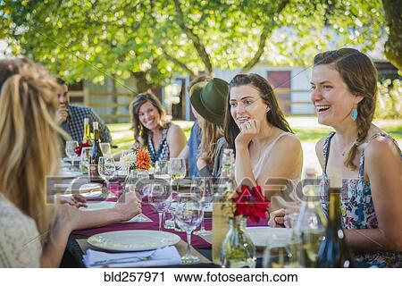 Stock Image - Caucasian women talking at table at party outdoors. Fotosearch