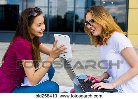Stock Image - Caucasian women using laptop and digital tablet outdoors. Fotosearch