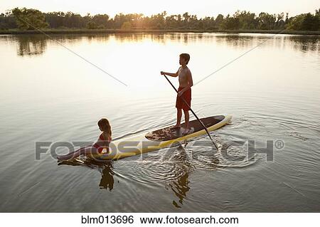 Stock Photograph - Children on paddleboard on lake. Fotosearch
