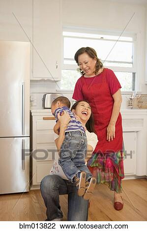 Stock Image - Chinese family laughing in kitchen. Fotosearch