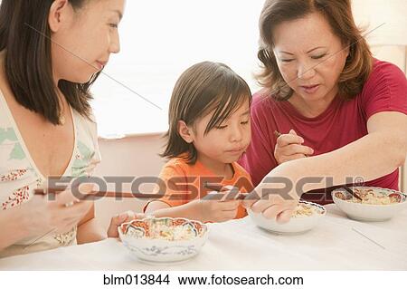 Picture - Chinese grandmother teaching grandson to use chopsticks. Fotosearch