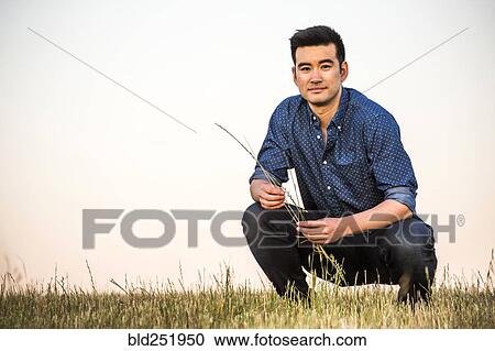 Chinese man crouching in field holding grass View Large Photo Image Stock Image - Chinese man crouching in field holding grass. Fotosearch