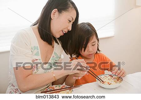 Stock Image - Chinese mother teaching son to use chopsticks. Fotosearch