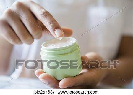 Stock Photo - Close up of African American woman dipping finger in lotion jar. Fotosearch