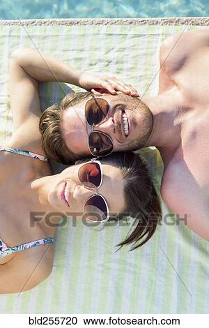 Stock Image - Close up of Caucasian couple laying near swimming pool. Fotosearch