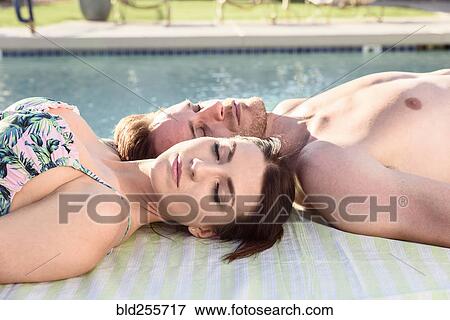 Stock Photo - Close up of Caucasian couple laying near swimming pool. Fotosearch