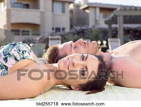 Stock Photo - Close up of Caucasian couple laying near swimming pool. Fotosearch