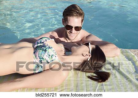 Stock Image - Close up of Caucasian couple relaxing at swimming pool. Fotosearch